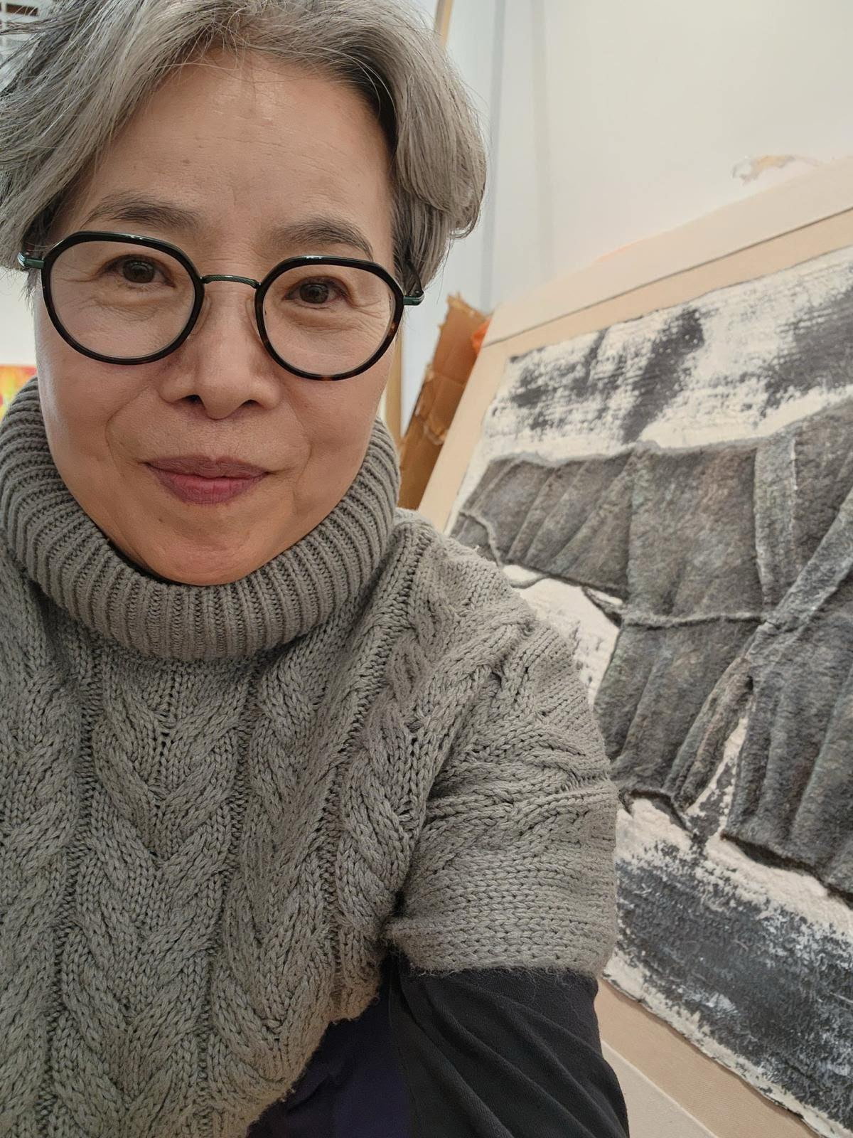 Artist Hyungjoo Kim in her studio beside a black-and-white work.